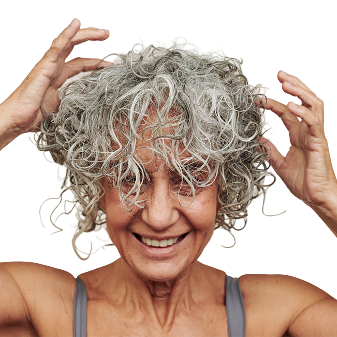 Woman with curly gray hair touching her hair against a neutral background