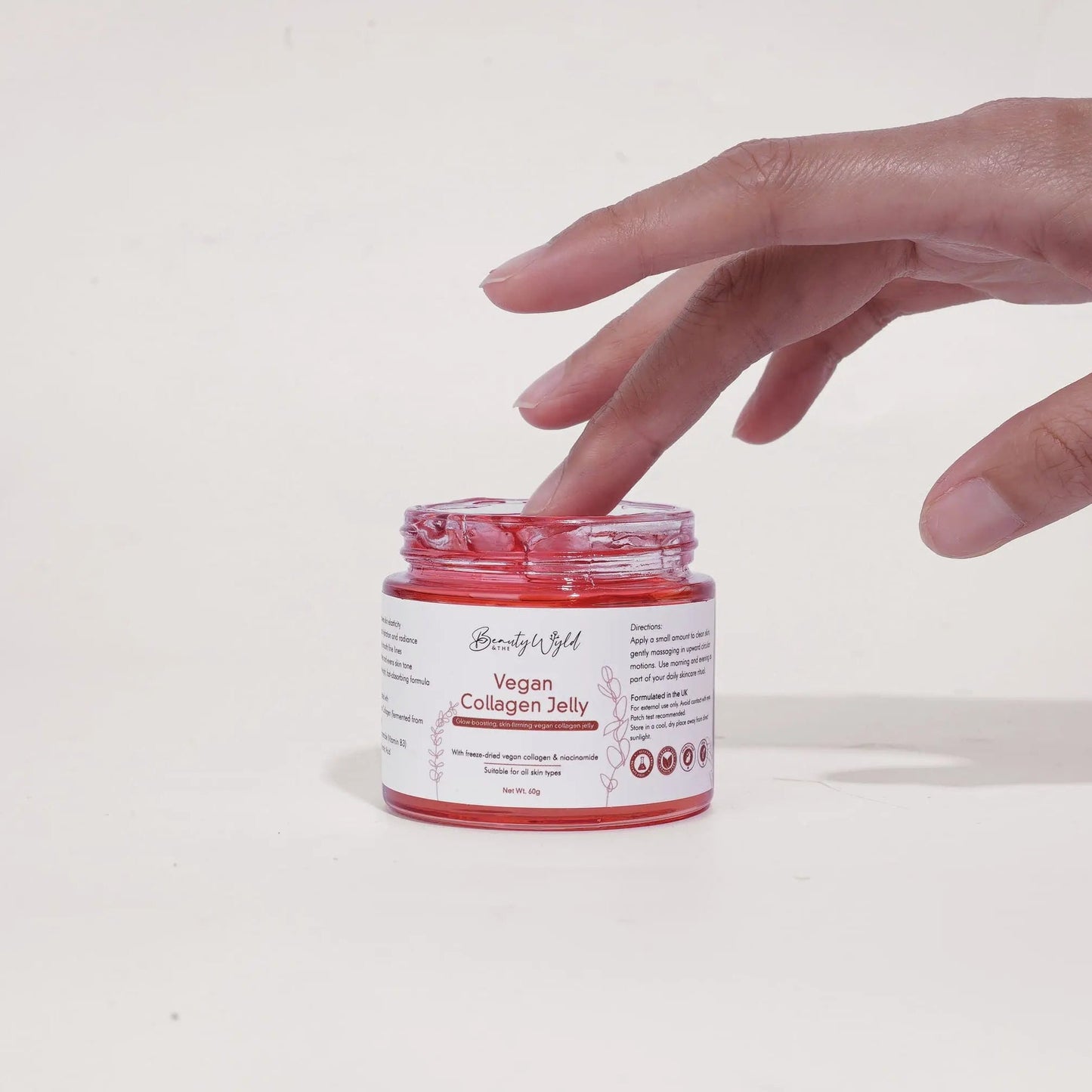 Hand reaching towards a jar of pink vegan collagen jelly on a white background