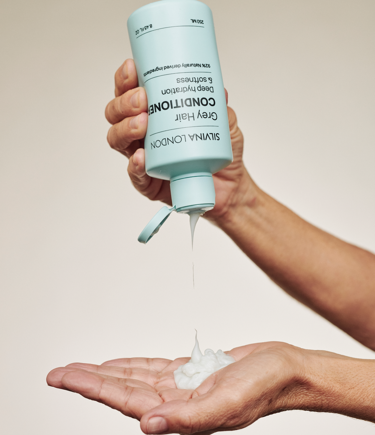 Person pouring a blue bottle of Silvian London conditioner into their hand against a neutral background
