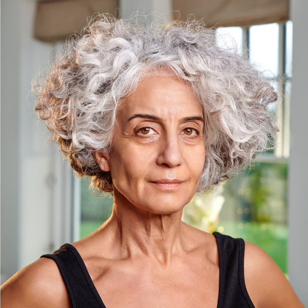 Woman with gray hair looking directly at the camera in a blurred indoor setting
