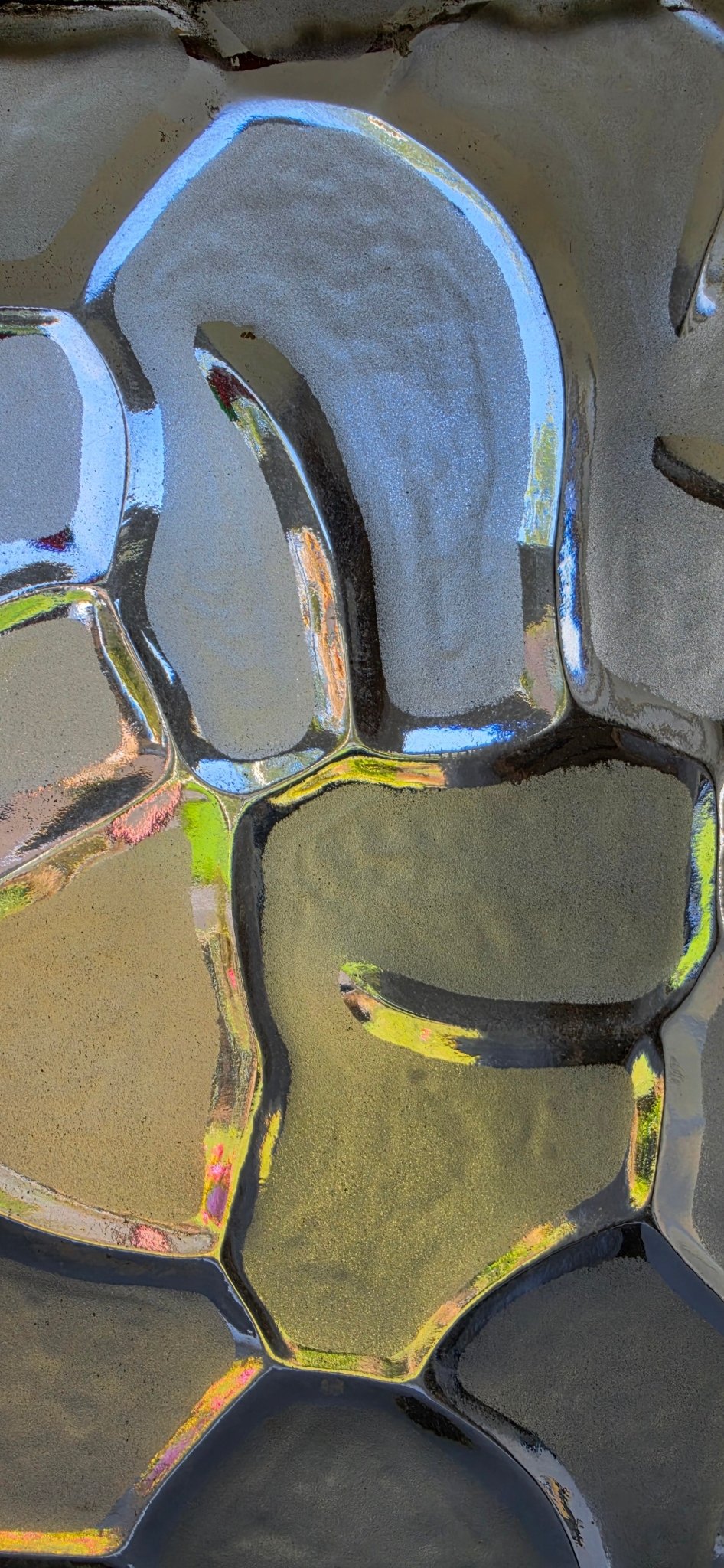 Close-up of "puzzle" glass pattern with vibrant iridescent reflections of blue, yellow, and green light.
