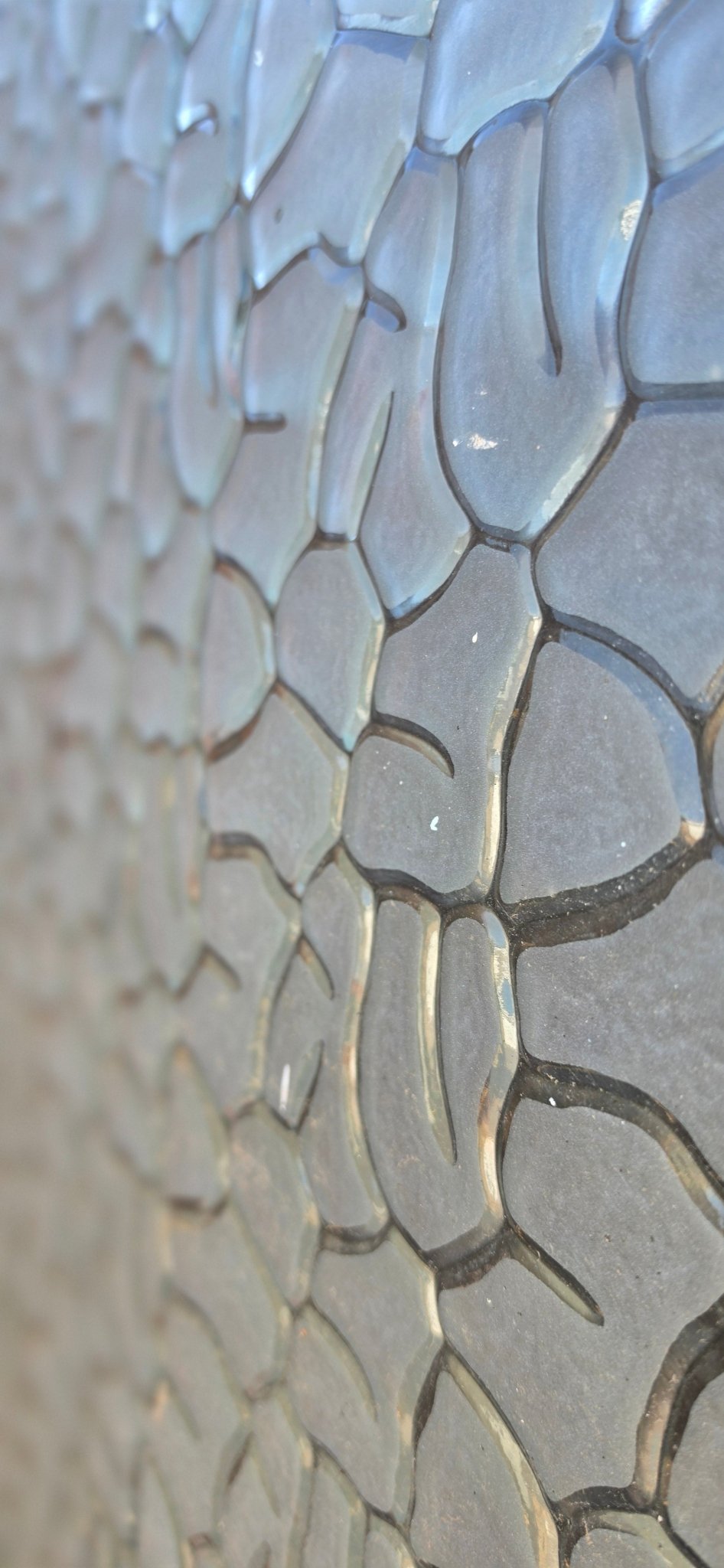 Detailed close-up of glass texture, highlighting dark recessed lines and smooth, raised grey-blue shapes.