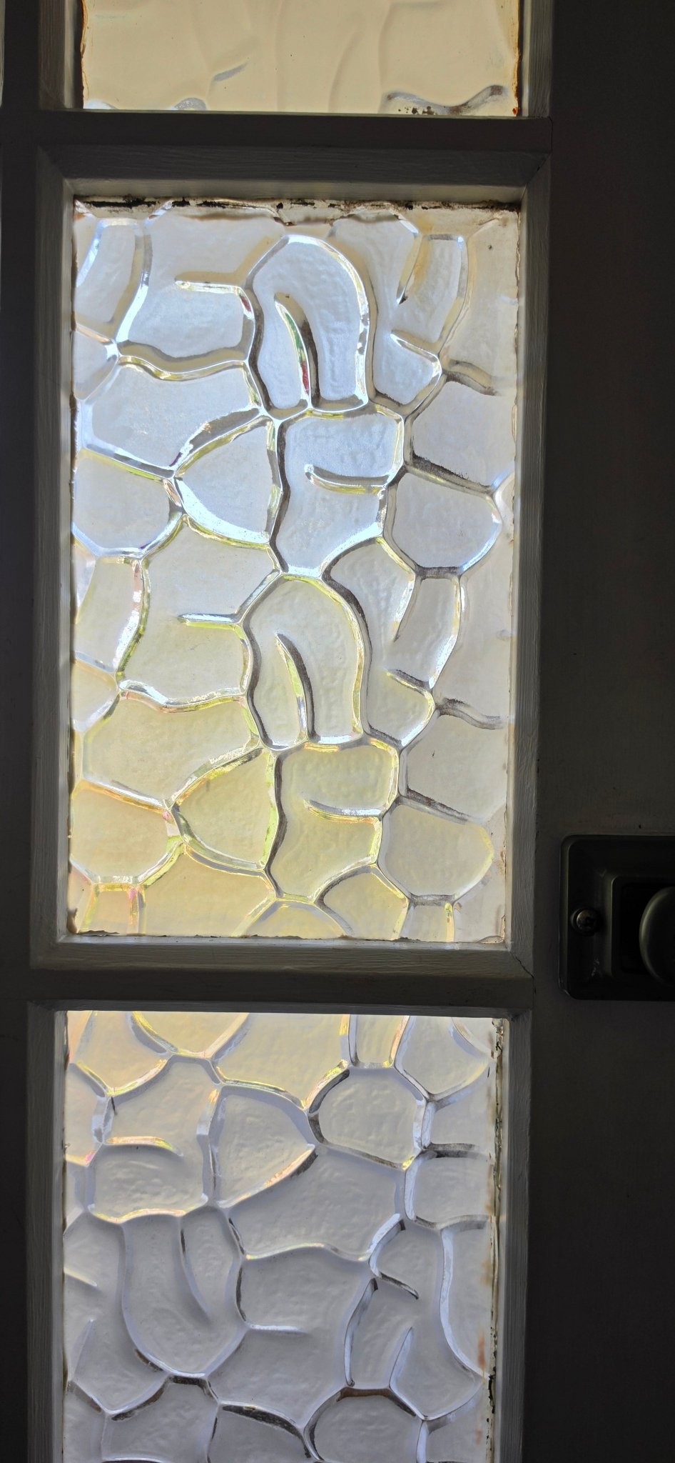 Three vertical panels of textured obscure glass in a door, glowing with sunlight and subtle iridescent colours.